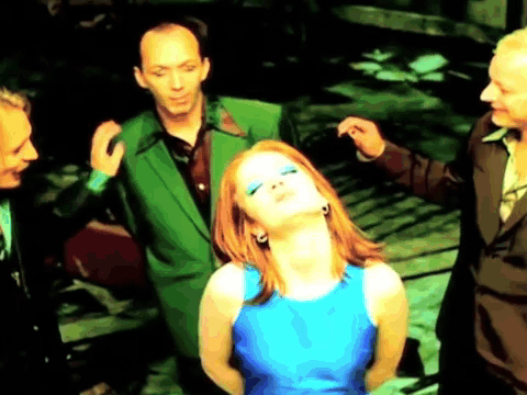A Woman In A Blue Dress Is Surrounded By Men In Green Suits . GIF