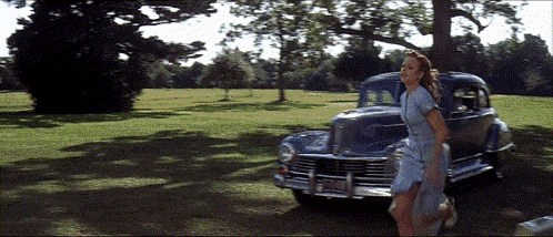 A Woman In A Blue Dress Is Walking In Front Of A Car With A License Plate That Says Jcj - 88 GIF