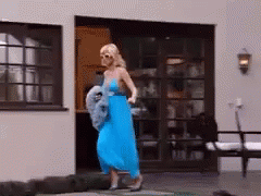 A Woman In A Blue Dress Is Walking In Front Of A House GIF