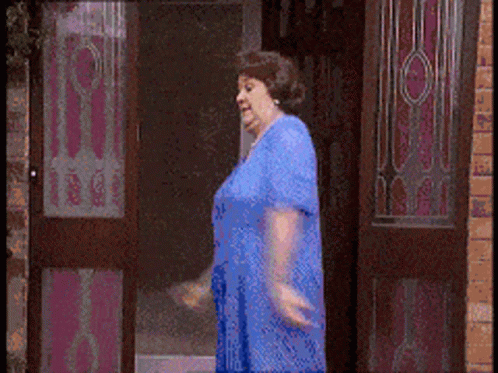 A Woman In A Blue Dress Is Walking Through A Door GIF