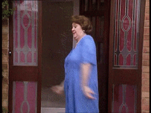 A Woman In A Blue Dress Is Walking Through A Doorway GIF