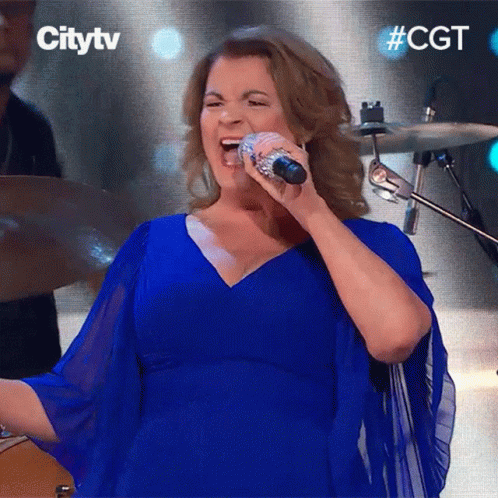 A Woman In A Blue Dress Sings Into A Microphone GIF