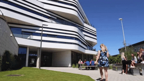 A Woman In A Blue Dress Stands In Front Of A Large Building GIF