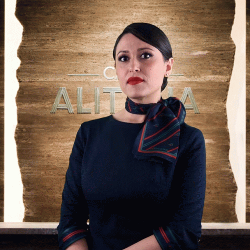 A Woman In A Blue Dress Stands In Front Of A Sign That Says Alit GIF