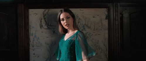 A Woman In A Blue Dress Stands In Front Of A Wall With Drawings On It GIF