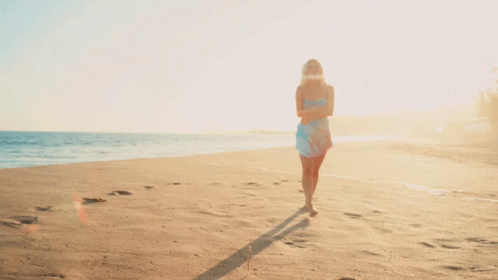 A Woman In A Blue Dress Walking On A Beach GIF