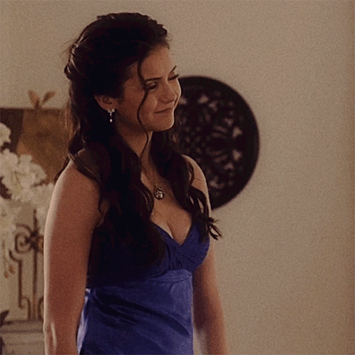 A Woman In A Blue Dress With A Plunging Neckline And Earrings GIF