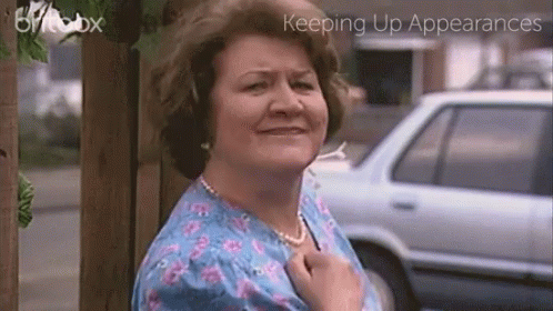 A Woman In A Blue Floral Shirt Is Standing In Front Of A Car With The Words Keeping Up Appearances On The Bottom GIF