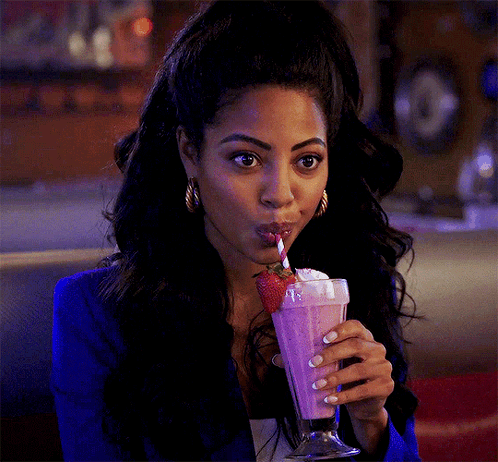 A Woman In A Blue Jacket Is Drinking A Pink Milkshake With Whipped Cream And Strawberries . GIF
