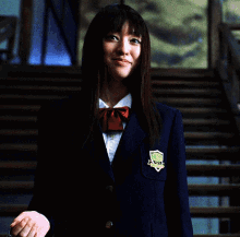 A Woman In A Blue Jacket Is Holding A Chain Around Her Neck And Smiling GIF