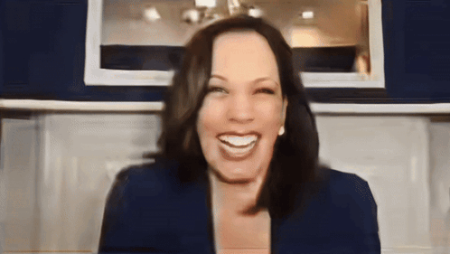 A Woman In A Blue Jacket Is Smiling In Front Of A Blue Wall GIF