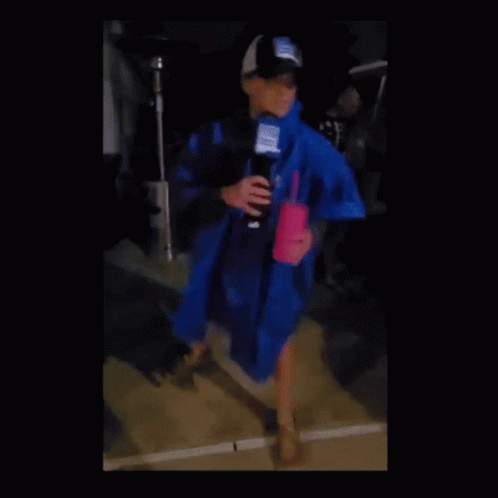 A Woman In A Blue Raincoat Holding A Microphone And A Pink Cup GIF
