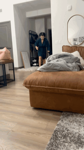 A Woman In A Blue Robe Is Standing In A Living Room GIF