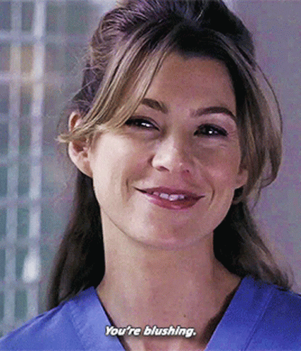 A Woman In A Blue Scrub Top Is Smiling And Saying You 'Re Blushing . GIF