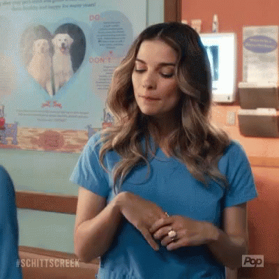 A Woman In A Blue Scrub Top Is Standing In Front Of A Poster Of A White Dog . GIF