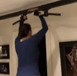 A Woman In A Blue Shirt Is Doing A Pull Up On A Bar . GIF
