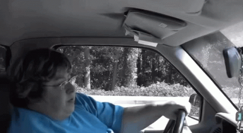 A Woman In A Blue Shirt Is Driving A Car With The Number 2 On The Steering Wheel GIF