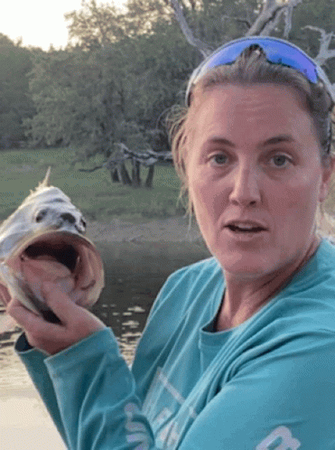 A Woman In A Blue Shirt Is Holding A Fish GIF