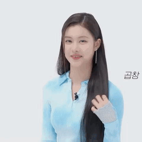 A Woman In A Blue Shirt Is Holding Her Hair And Smiling . GIF