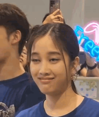 A Woman In A Blue Shirt Is Making A Funny Face While Sitting In A Crowd . GIF