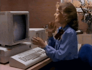 A Woman In A Blue Shirt Is Sitting At A Desk In Front Of An Old Computer . GIF
