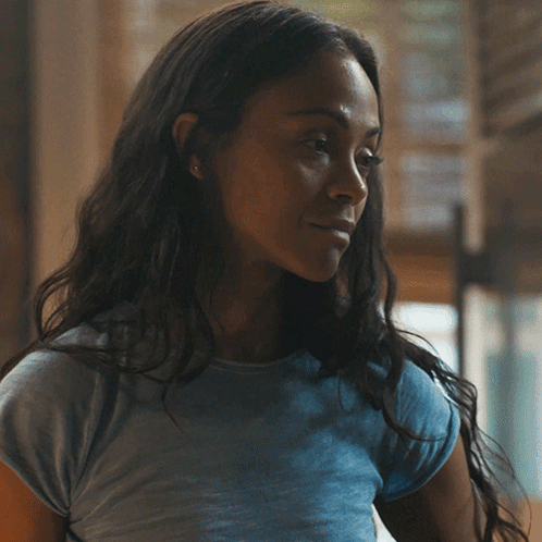 A Woman In A Blue Shirt Is Smiling And Looking At The Camera GIF