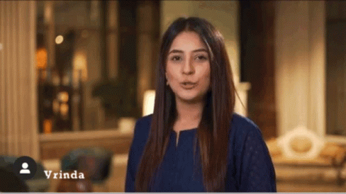 A Woman In A Blue Shirt Is Standing In A Living Room With The Name Vrinda On The Bottom GIF
