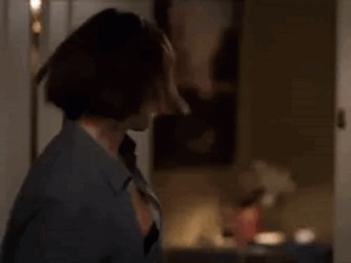A Woman In A Blue Shirt Is Standing In A Room Holding A Bottle Of Wine . GIF