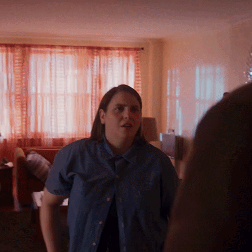 A Woman In A Blue Shirt Is Standing In A Room GIF