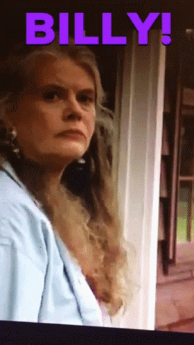A Woman In A Blue Shirt Is Standing In Front Of A Door And The Word Billy Is On The Screen GIF