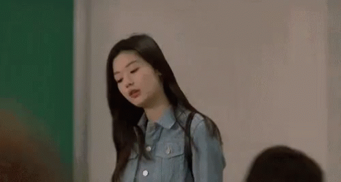 A Woman In A Blue Shirt Is Standing In Front Of A Green Wall . GIF