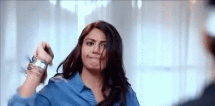 A Woman In A Blue Shirt Is Standing In Front Of A Mirror Holding Her Hair . GIF