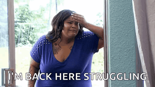 A Woman In A Blue Shirt Is Standing In Front Of A Window And Covering Her Forehead With Her Hand . GIF