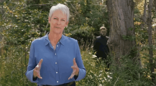 A Woman In A Blue Shirt Stands In A Forest GIF
