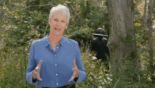 A Woman In A Blue Shirt Stands In The Woods GIF