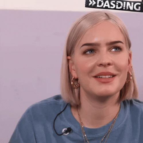 A Woman In A Blue Shirt With A Microphone Around Her Neck Is Smiling GIF