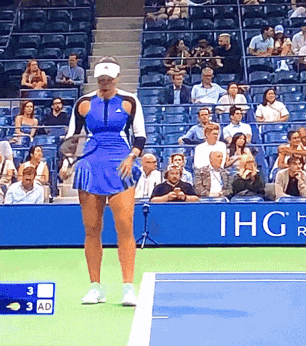 a woman in a blue skirt is standing on a tennis court in front of an ihg sign