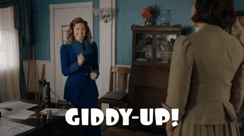 A Woman In A Blue Suit Is Standing Next To Another Woman In A Green Dress And The Words Giddy-Up Are Visible GIF