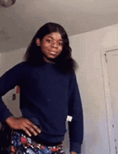 A Woman In A Blue Sweater And Floral Pants Is Standing With Her Hands On Her Hips . GIF