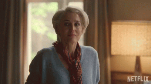 A Woman In A Blue Sweater And Scarf Stands In Front Of A Netflix Sign GIF