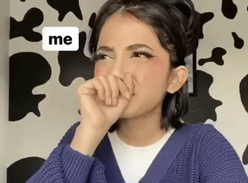 A Woman In A Blue Sweater Is Covering Her Mouth With Her Hand In Front Of A Cow Print Wall . GIF