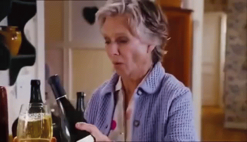 A Woman In A Blue Sweater Is Holding A Bottle Of Wine And A Glass Of Wine . GIF