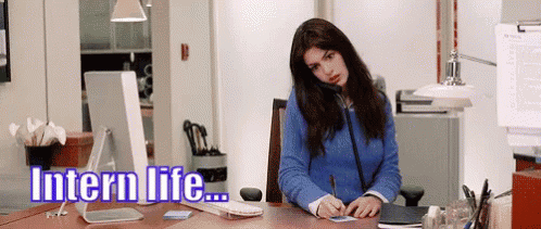 A Woman In A Blue Sweater Is Sitting At A Desk In Front Of A Computer With The Words Intern Life Written Above Her GIF