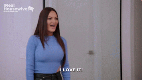 A Woman In A Blue Sweater Is Standing In Front Of A Door And Says I Love It . GIF