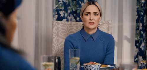 a woman in a blue sweater sits at a table with a plate of food