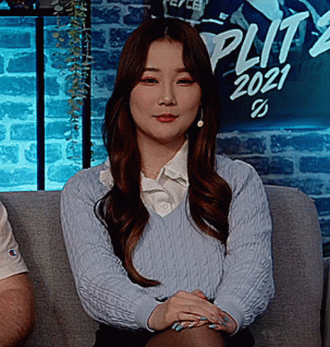 A Woman In A Blue Sweater Sits On A Couch In Front Of A Split 2021 Sign GIF
