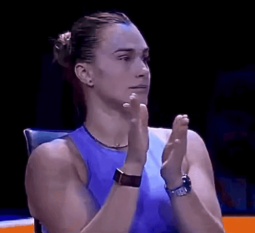 A Woman In A Blue Tank Top Is Clapping Her Hands In A Dark Room . GIF