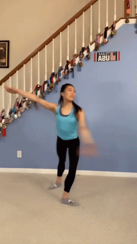 A Woman In A Blue Tank Top Is Dancing In Front Of A Sign That Says A2u GIF