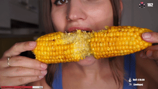 A Woman In A Blue Tank Top Is Eating Corn On The Cob With 162 In The Corner GIF