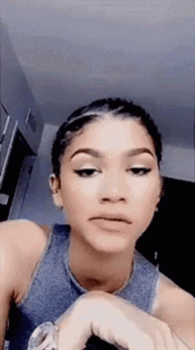A Woman In A Blue Tank Top Is Making A Funny Face While Looking At Her Watch . GIF